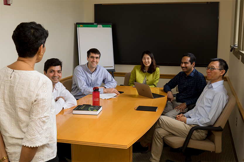 PhD student and four Johnson faculty sit around table while they listen to Nicholas H. Noyes Professor of Management, Vrinda Kadiyali, present
