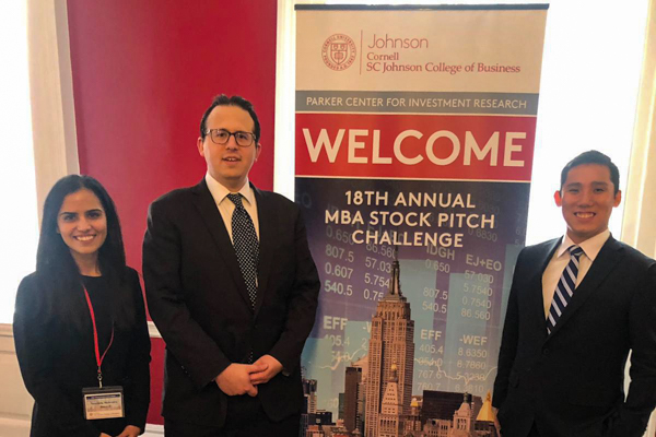 Three MBAs stand next to a welcome banner