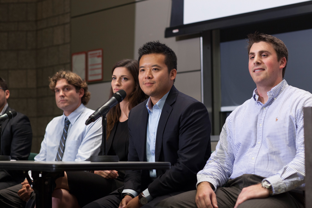 Students sitting on a stage in front of a microphone.