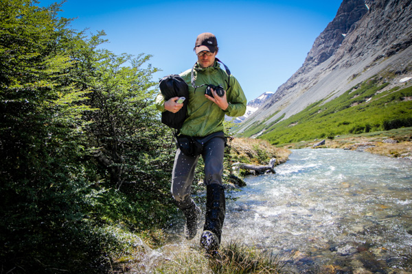 A man crosses a stream in a rugged landscape