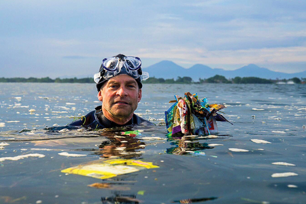 Fisk Johnson in a diving suit above water holding plastic waste in the ocean