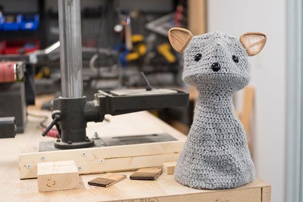 photo of a crocheted social robot that looks like a cat sitting in an engineering fabrication workshop