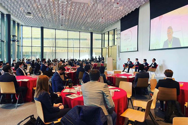 a room full of people dressed in business attire watch big screens at the front of the room