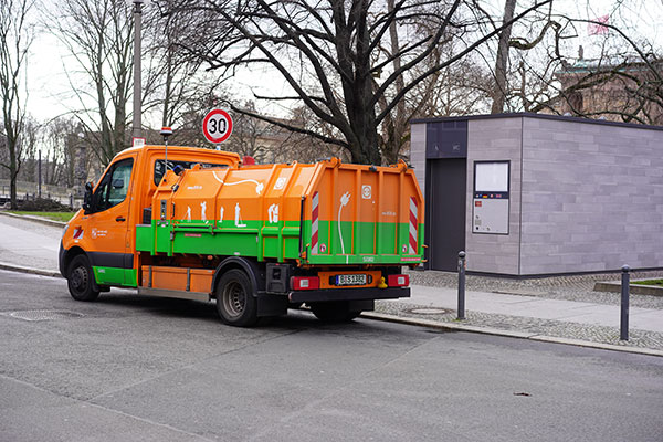 orange and green electric garbage truck with electric cord graphic on the side