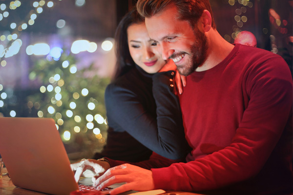 Couple standing together smiling while looking at a laptop