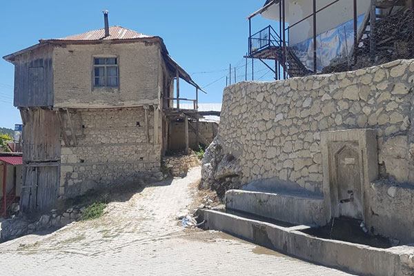 old, light grey stone building, wall, and road built on a steep incline.