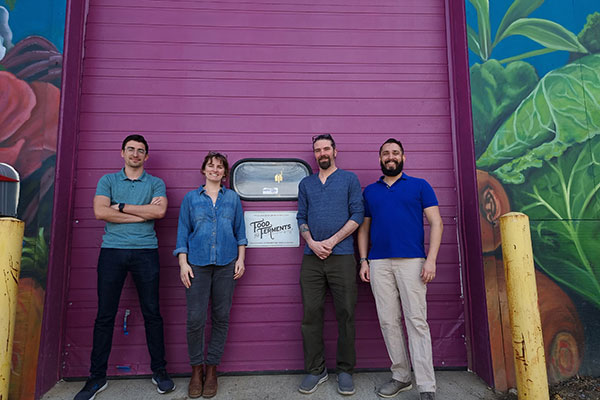 A picture of Adit Desai, Beto Durón, Dave Dougherty, and Carly Dougherty posing in front of a purple warehouse door.