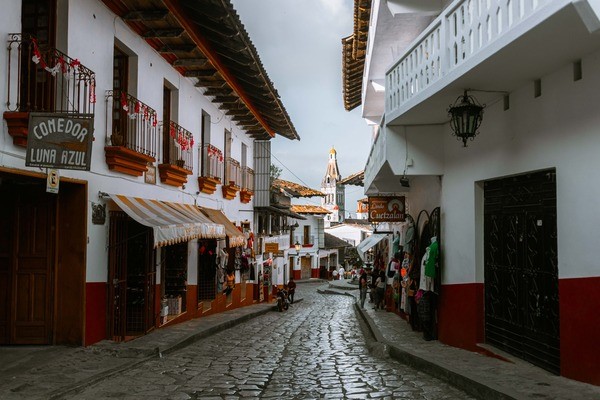A narrow, cobblestone street featuring red and white buildings and business signs in Spanish.