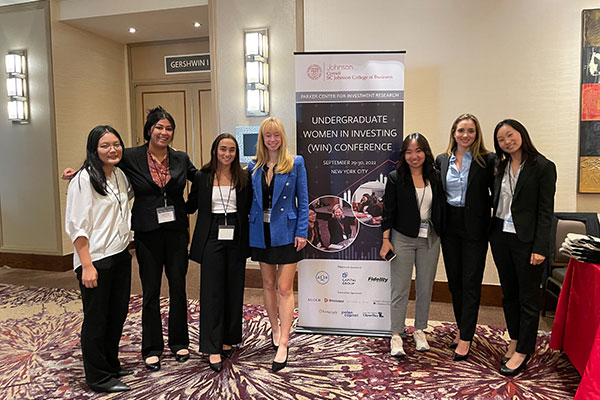 Woman students in business attire pose next to a WIN Conference banner.