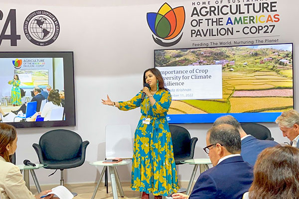 Kehkashan Basu speaking at the front of a room with a backdrop banner: Home of Sustainable Agriculture of the Americas Pavilion COP27.