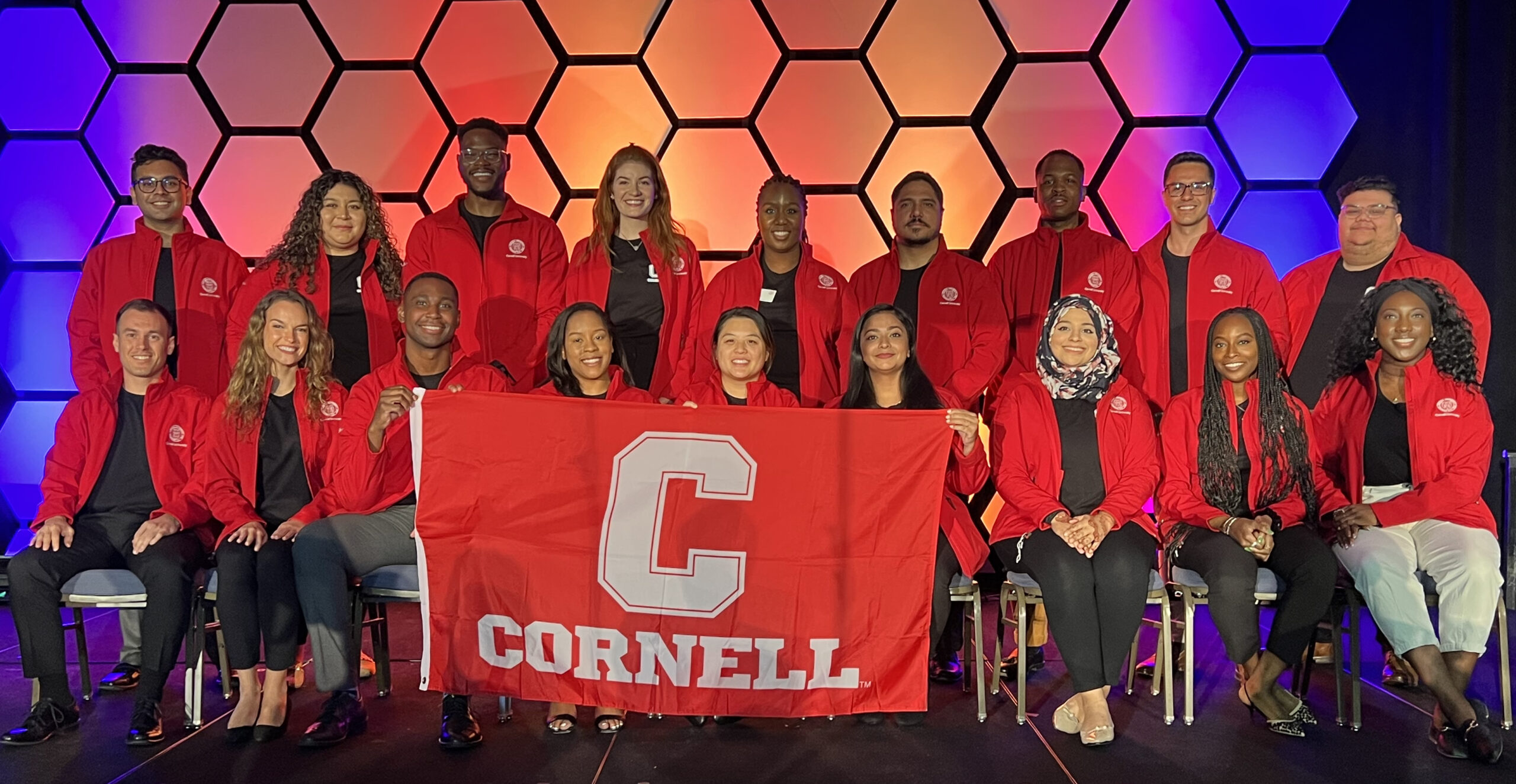 Group of people in read jackets holding a Cornell flag