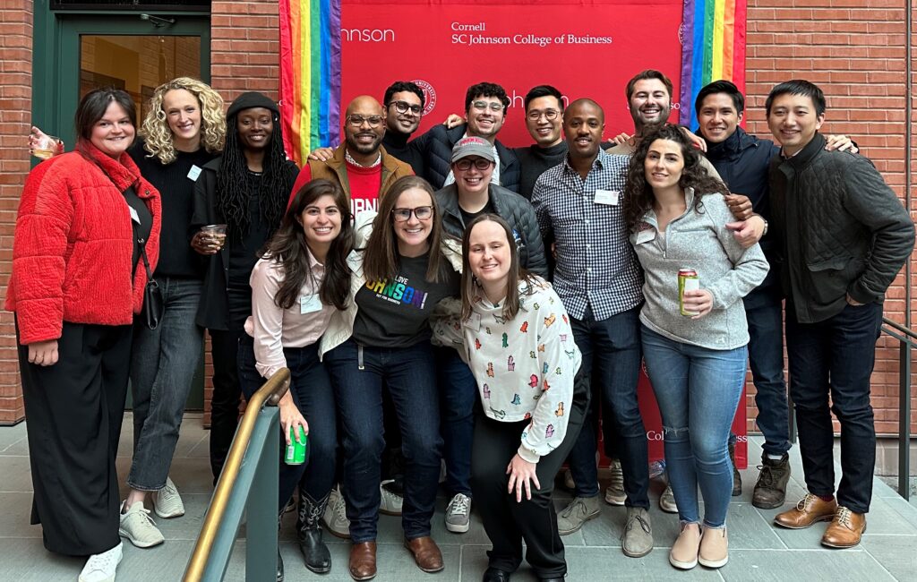 A group of students posing in front of a Johnson banner with rainbow flags.