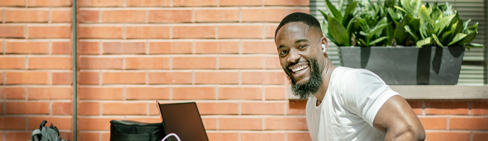 A male student with airpods in his ears smiles in front of a laptop.