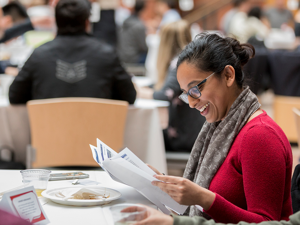 Woman sitting at a table reading a printed document.