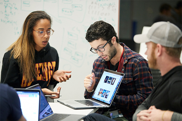 Three people huddle around a laptop.