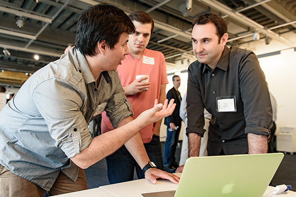 Three people gather around a laptop in discussion.