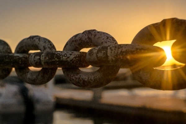 links of a large metal chain with the rising or setting sun shining through one of the links.