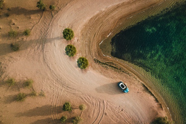 an aerial view of single car on a sandy dirt road.