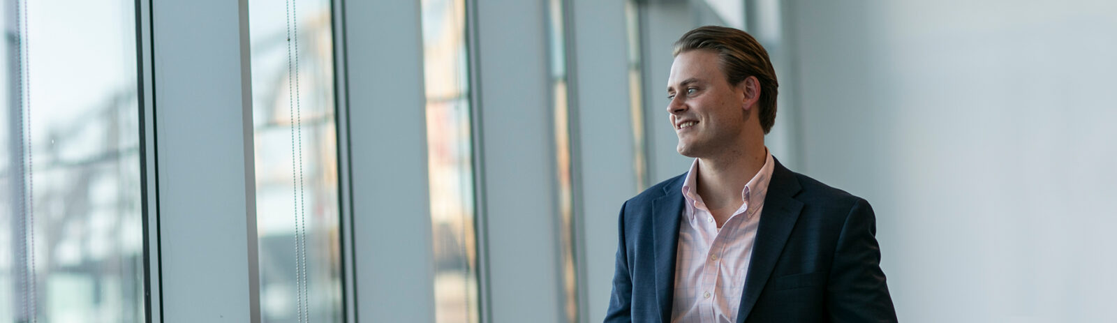 A man in a suit smiles as he looks out a wall of windows.