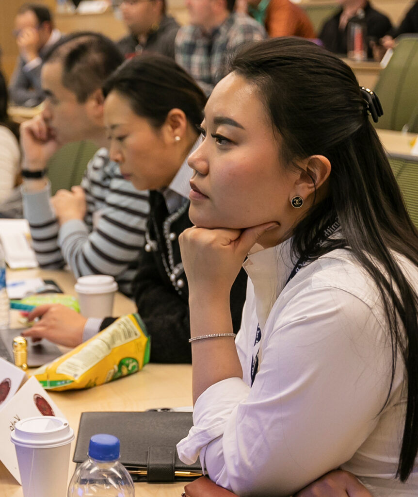 A woman sits in a tiered classroom resting her chin on her hand.