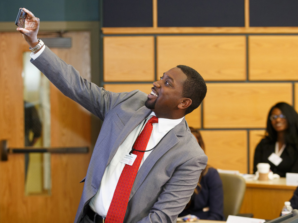 Eddie Asbie takes a selfie of himself and people sitting in a tiered classroom.