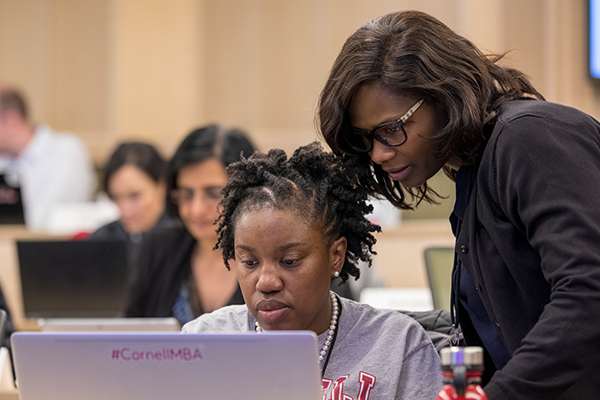 A student sit in front of a laptop while a professor stands and looks at the screen with them.