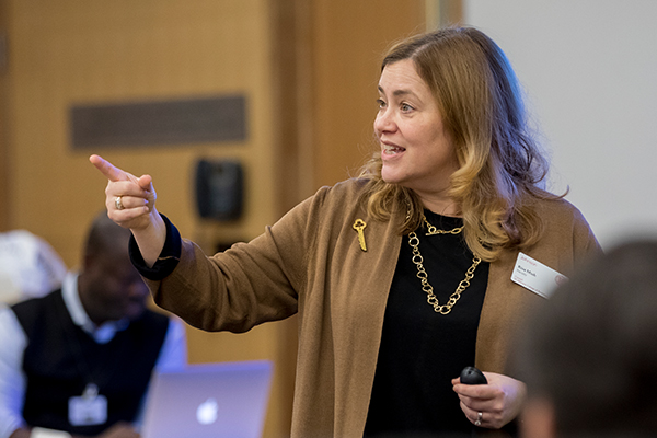 A female professor stands at the front of a classroom and points out of frame.