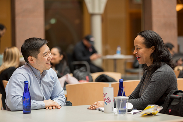 Two people sit at a table chatting in the atrium of Sage Hall.