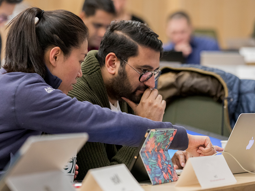 Two students sit and collaborate in front of a laptop.