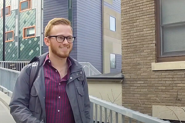 Jim walks down the sidewalk with a backpack on his back.