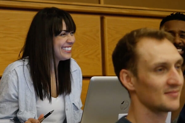 Lucie smiles broadly while seated behind a laptop.