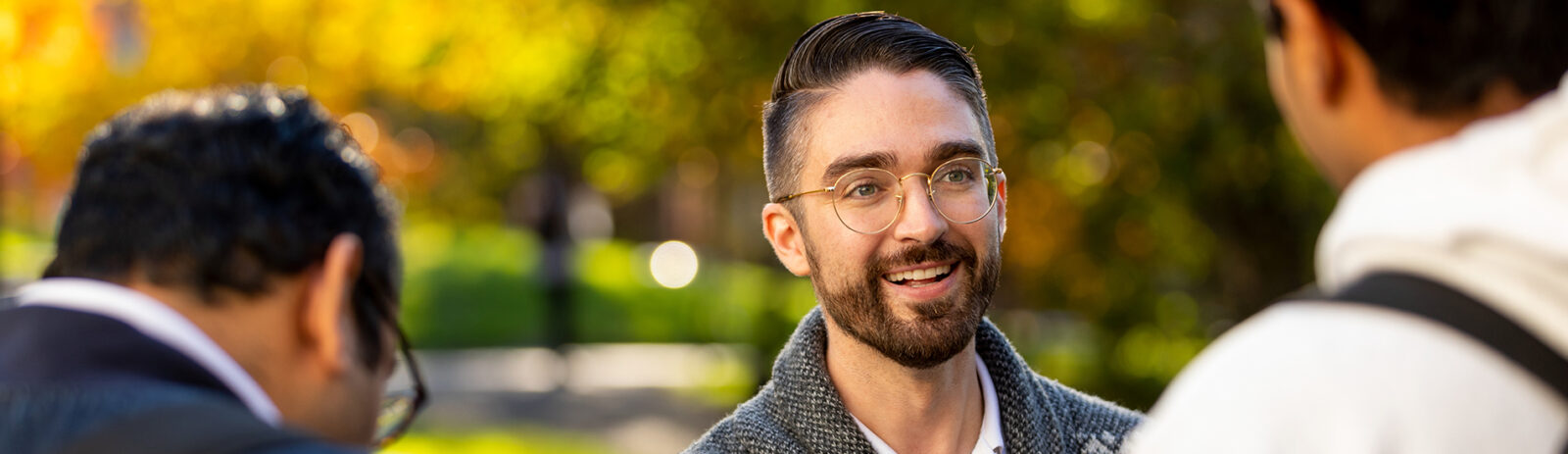 A student wearing glasses looks toward the camera with the back of two peoples heads in the foreground.