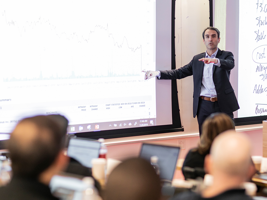 Professor pointing to a graph on a projector screen and speaking to a classroom.