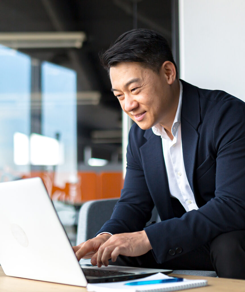 A man in a button-up shirt and a suit jacket types on a laptop.