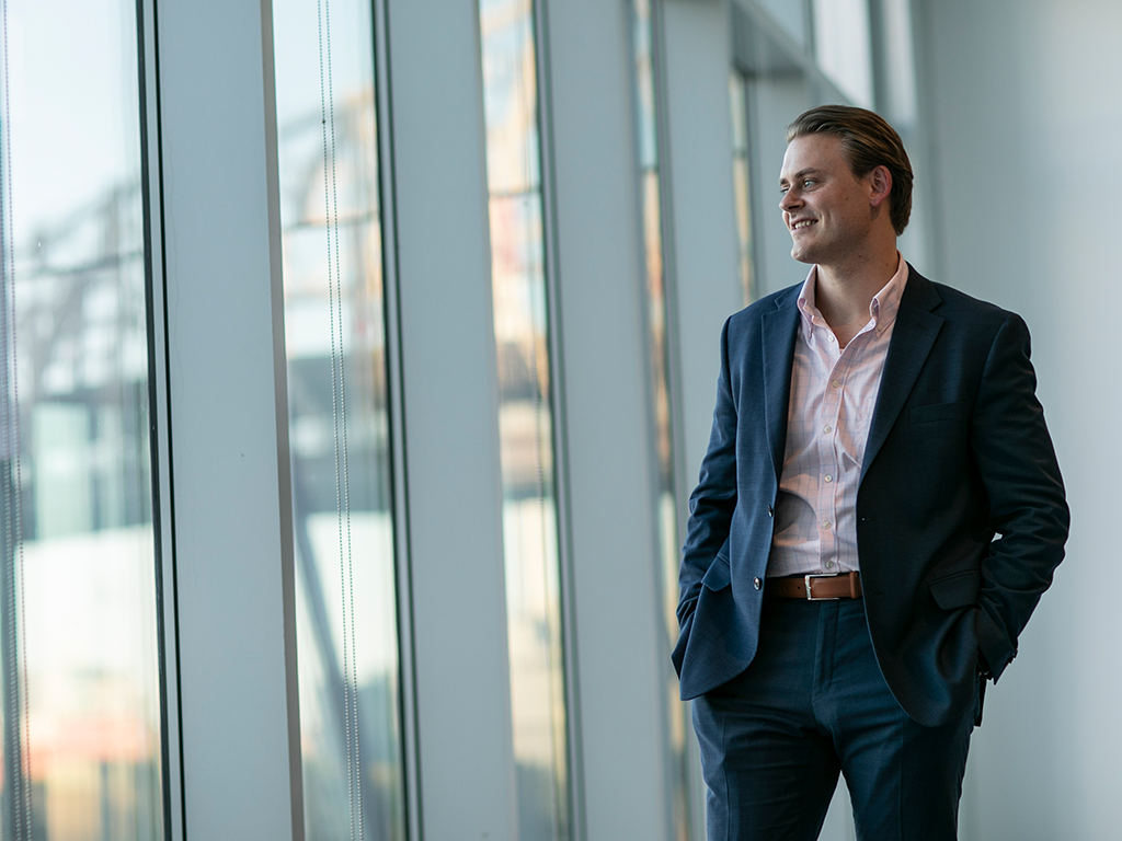 A man in a suit smiles as he looks out a wall of windows.