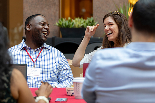 Two people sit at a table chatting in the atrium of Sage Hall.