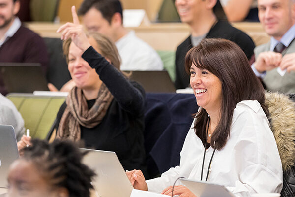 Students sit in a tiered classroom with laptops open in front of them.