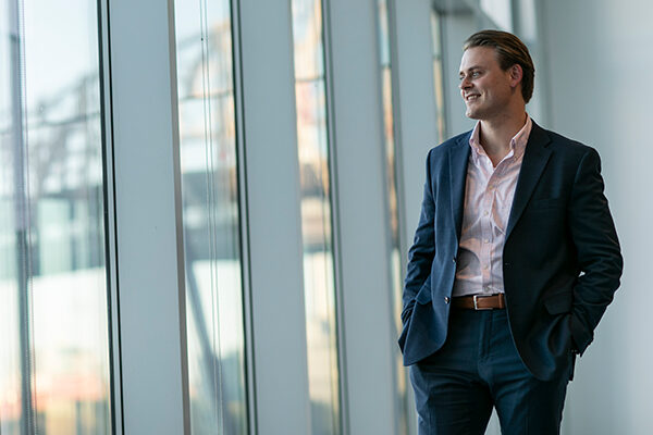 A man in a suit smiles as he looks out a wall of windows.