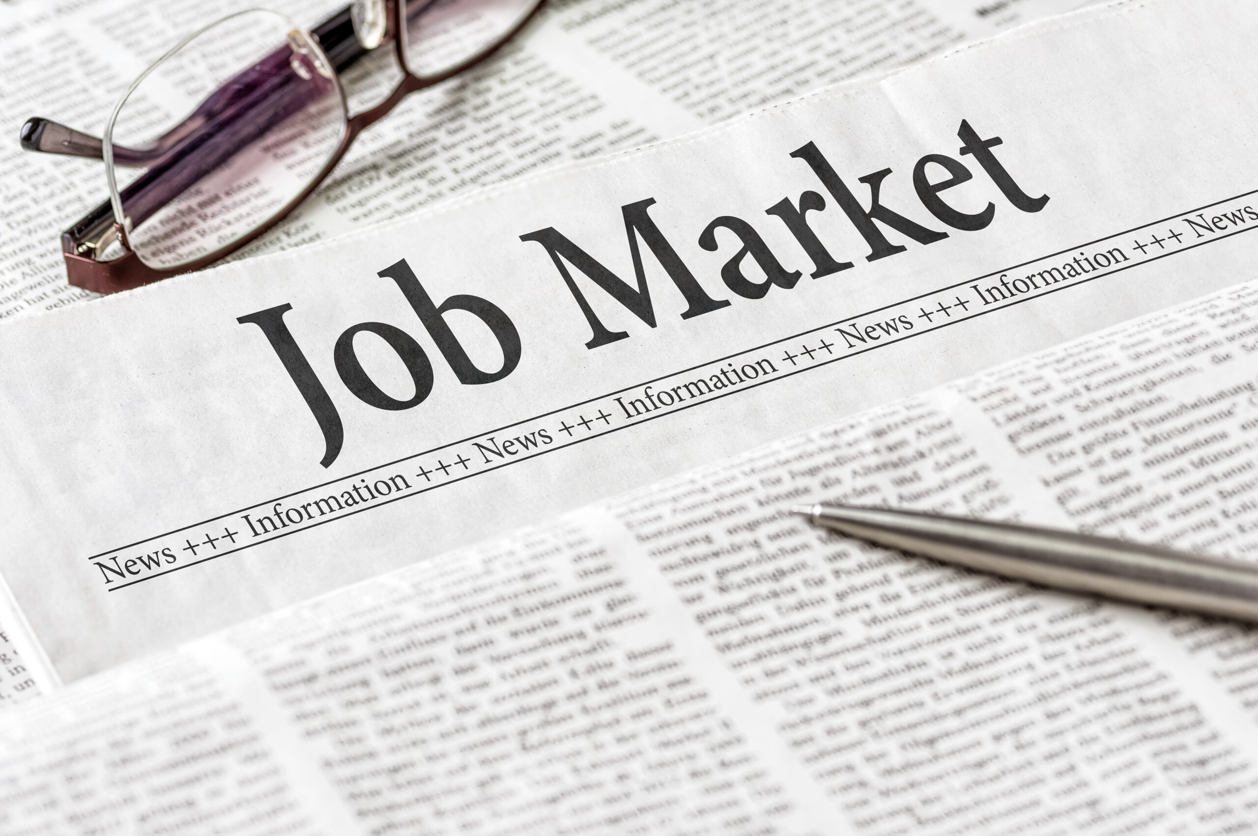 A newspaper with the headline Job Market, with glasses and a pen on top.