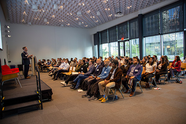 a speaker on a platform stage speaks to full room of people.