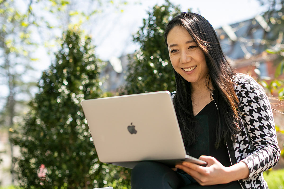 A woman sits outside smiling at a laptop screen.