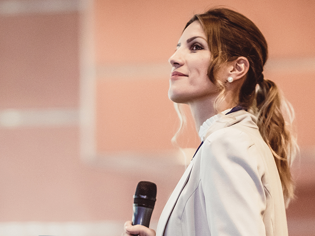 A woman in a blazer holds a microphone and looks to her left.