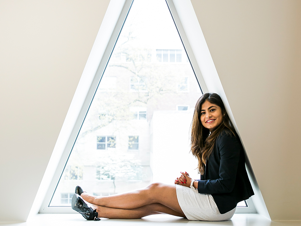 A woman in business attire sits on the windowsill of a triangle shaped window.
