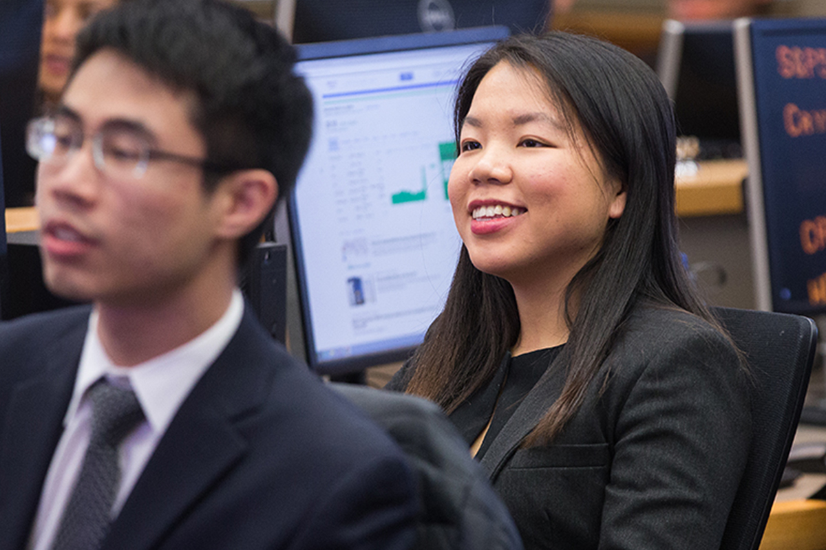 Two people in business attire sitting in front of desktop computers.