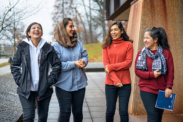 4 women standing and talking and smiling outside on the Cornell campus.