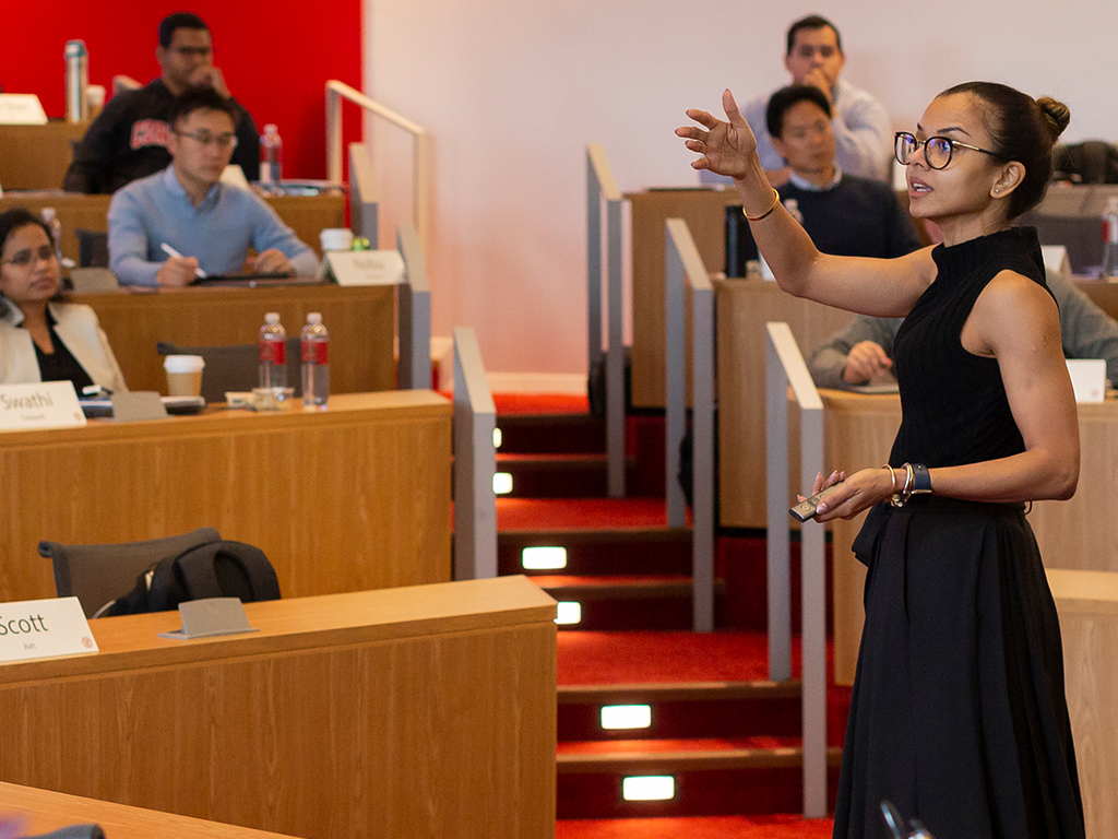 A professor speaks in front of a tiered classroom.