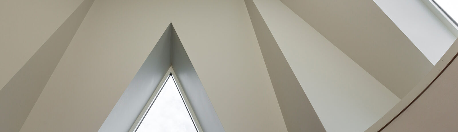 A triangle shaped window surrounded by cream colored walls.