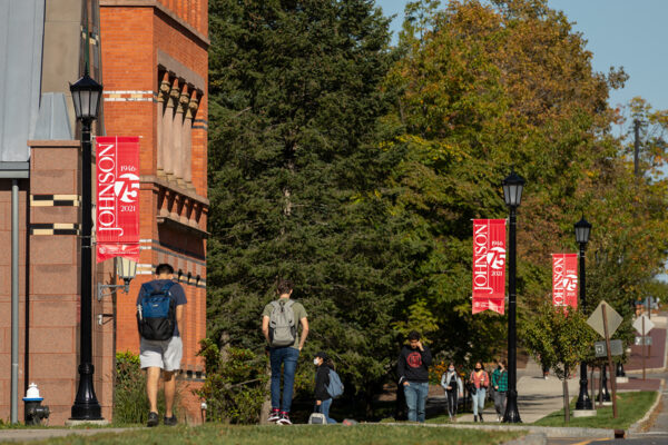 Students walk on the sidewalk outside of Sage Hall with “Johnson 75th Anniversary” banners on the light posts.