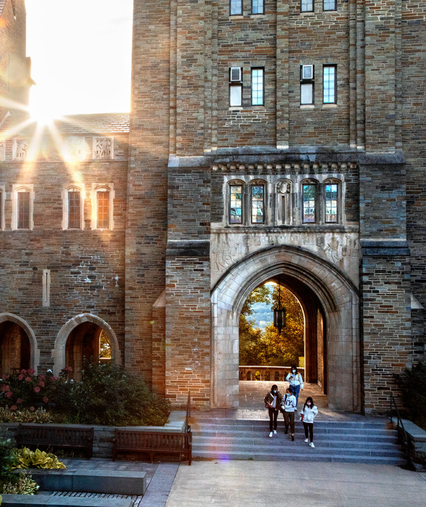 Four students walk out of a gray brick building as the sun shines from the left.