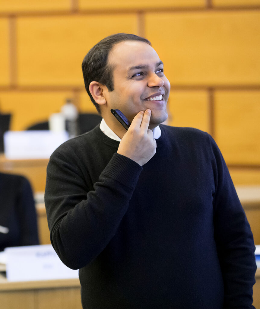 A man in a black sweater smiles and looks out of frame to the right.